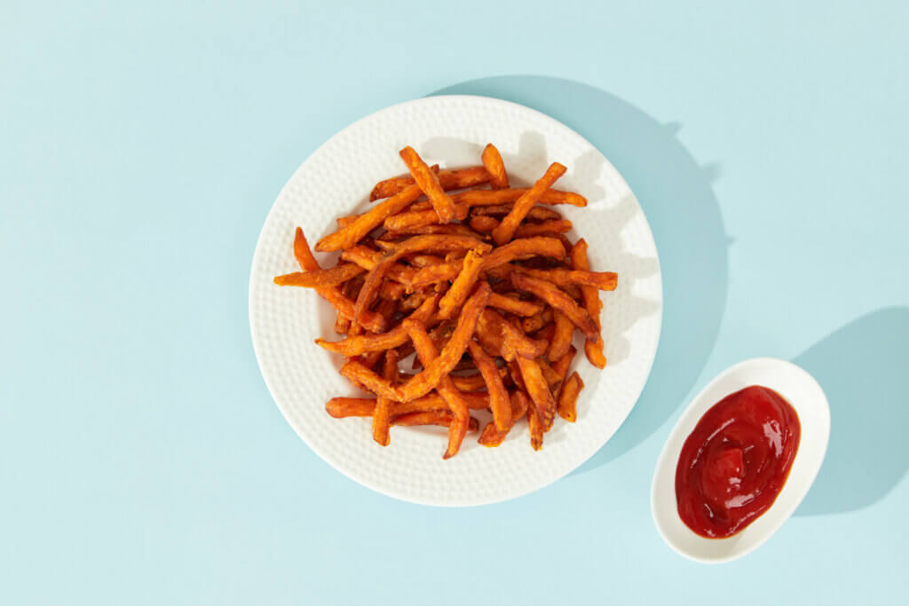 Sweet potato fries and sauce on blue background with long shadows in minimal style