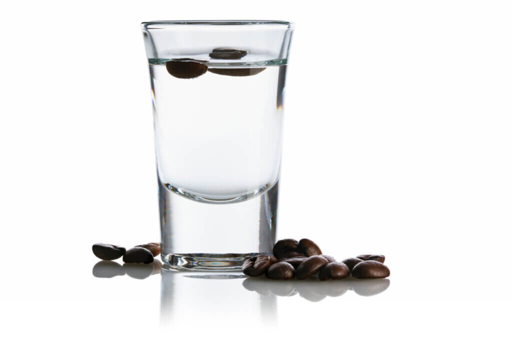 Sambuca in a shot glass surrounded by coffee beans, isolated on white background