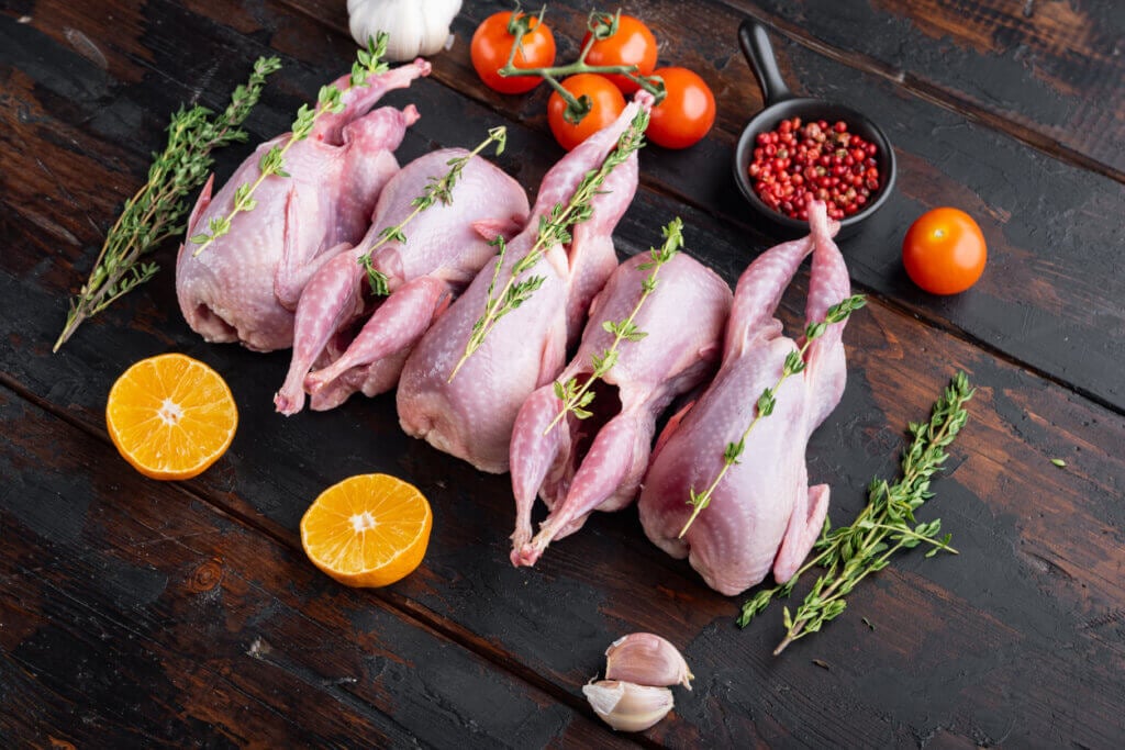 Fresh raw meat quails with herbs, on dark wooden background