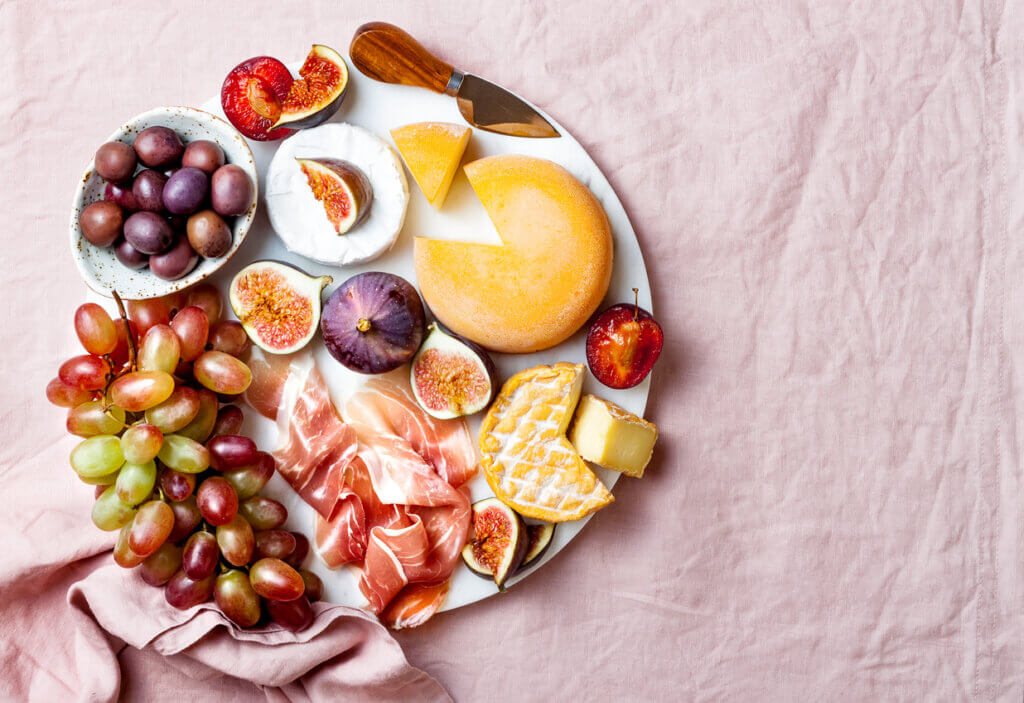 Appetizers, antipasti snacks. Cheese and fruit platter on marble board over pink linen tablecloth background.