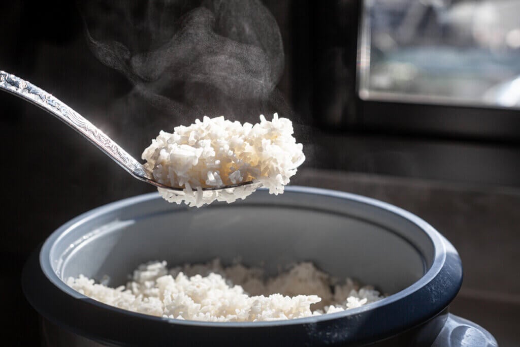 Jasmine rice cooking in electric rice cooker with steam on dark background.
