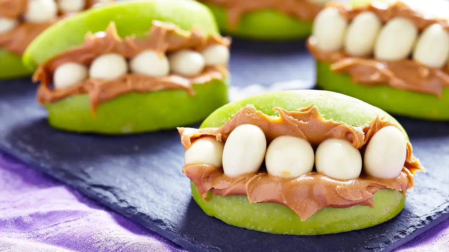 Apple slices with peanut butter and yogurt covered almonds that resemble teeth