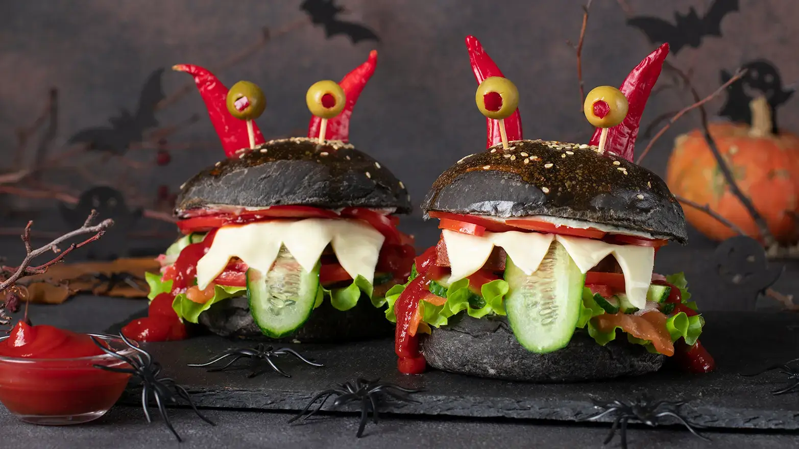 Monster burgers with black buns, olive eyes, and jagged cheese teeth