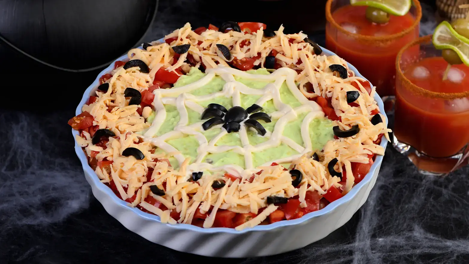 Seven layer dip with sour cream spider web on top with olive spider