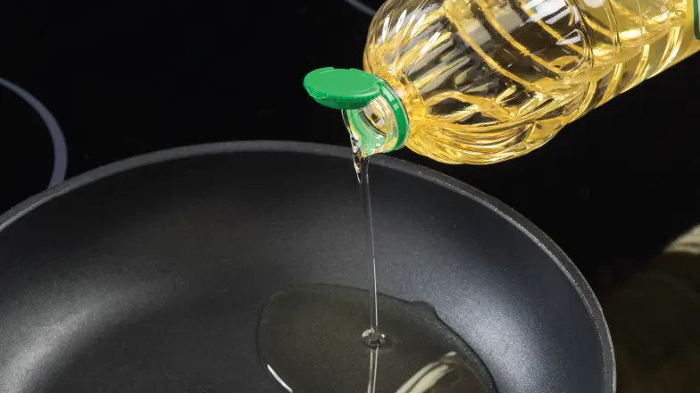 person pouring vegetable oil in a frying pan